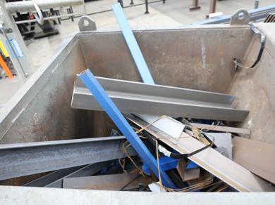 Mixed metal scrap and steel sections inside recycling bin.