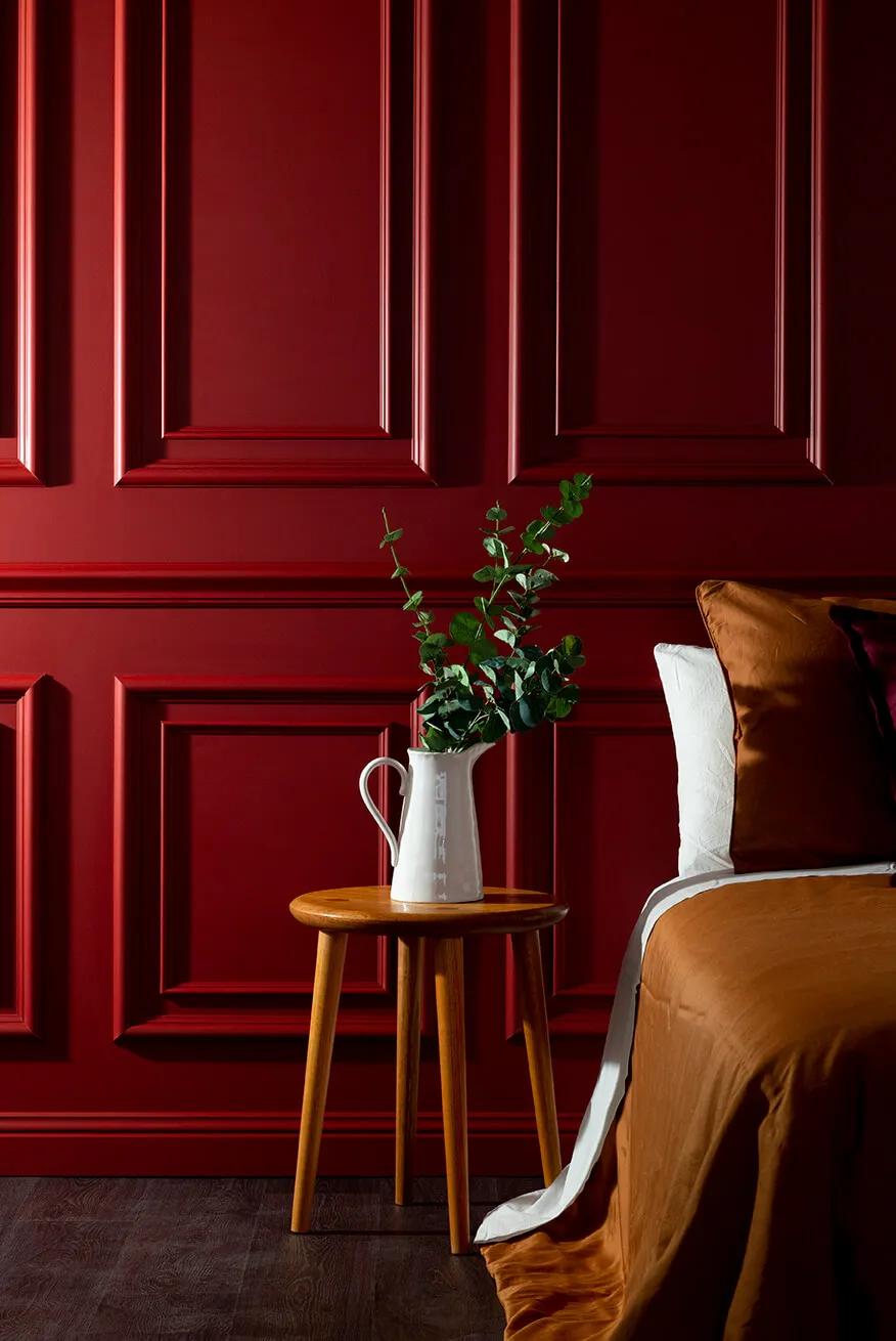 Bedroom with red paneled walls, wooden table with flowers on it, brown bedspread, and a vase