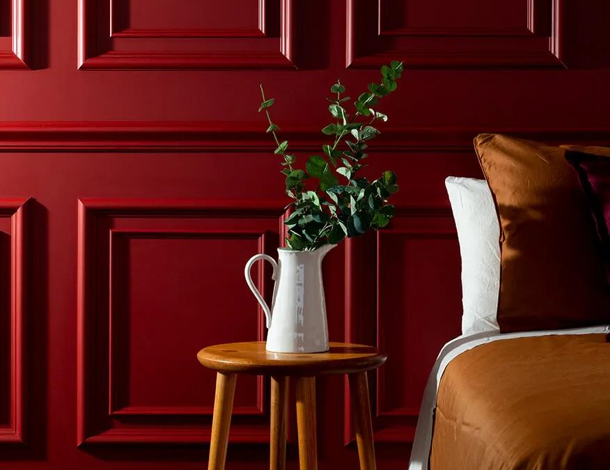 Bedroom with red paneled walls, wooden table with flowers on it, brown bedspread, and a vase