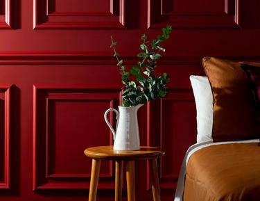 Bedroom with red paneled walls, wooden table with flowers on it, brown bedspread, and a vase
