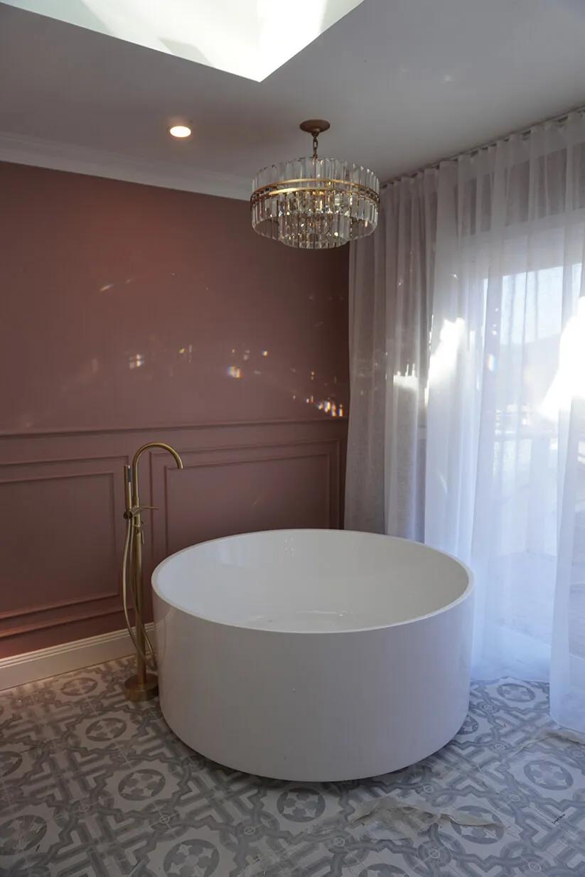 Large white bathtub, brown shower curtain, gold bathroom chandelier, white rug