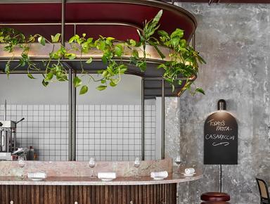A restaurant interior with a modern design featuring a counter with red stools, black bar stools, a wooden bar, a potted plant, a chalkboard menu, and shelves on the wall