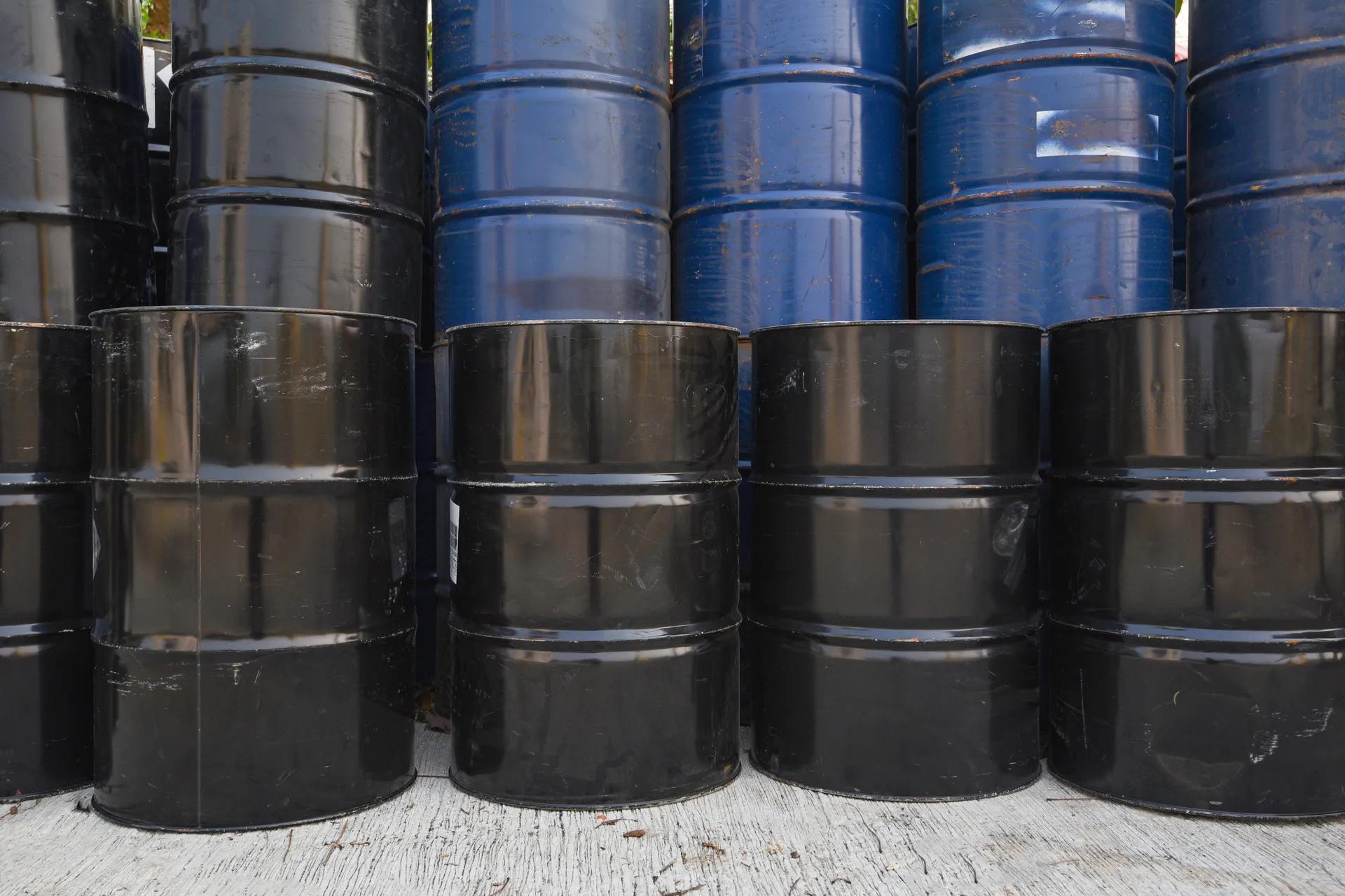 Stacked black and blue industrial liquid waste drums stored outdoors.