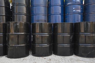 Stacked black and blue industrial liquid waste drums stored outdoors.
