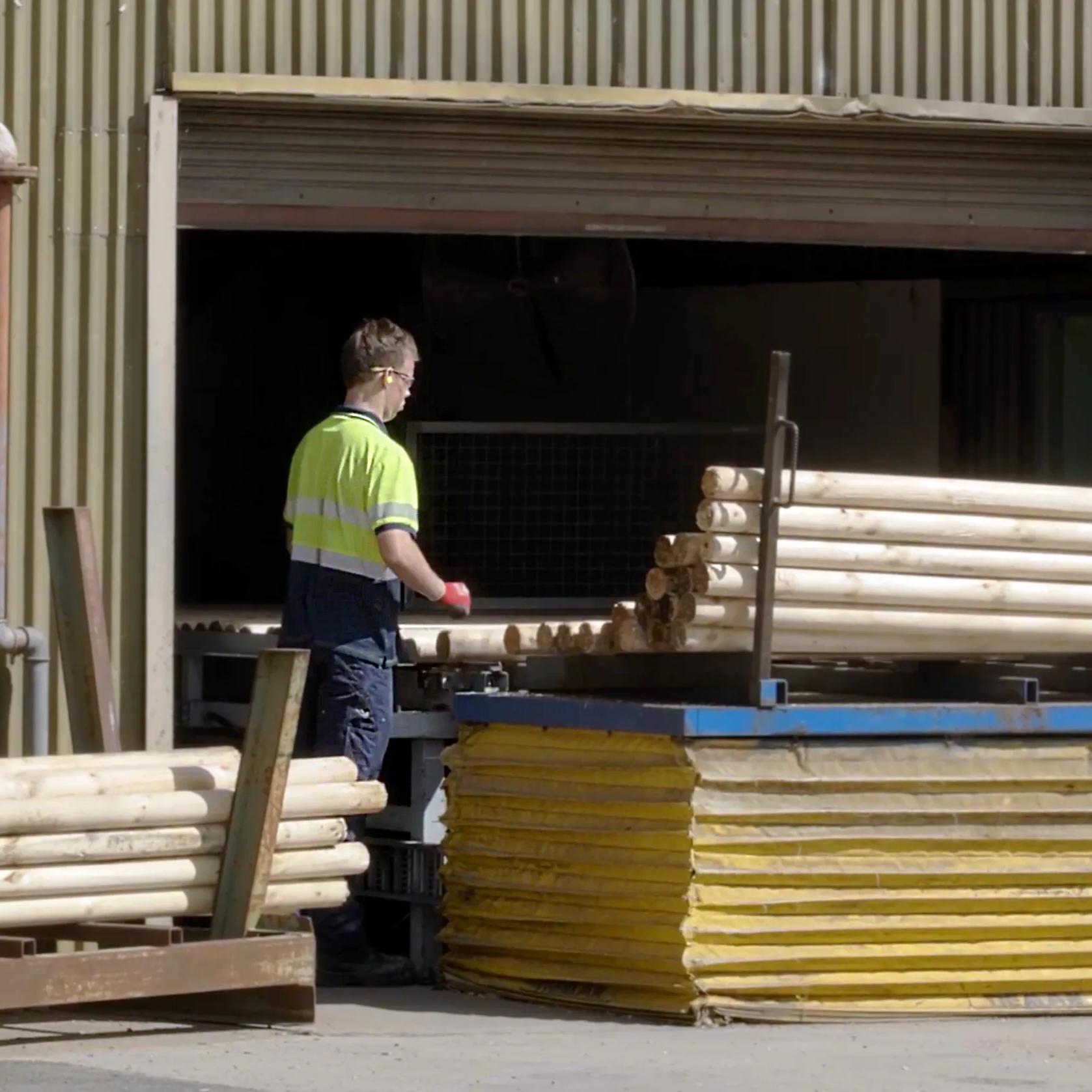 Worker handling stacked STRUCTAply sheets and timber poles outside an industrial building