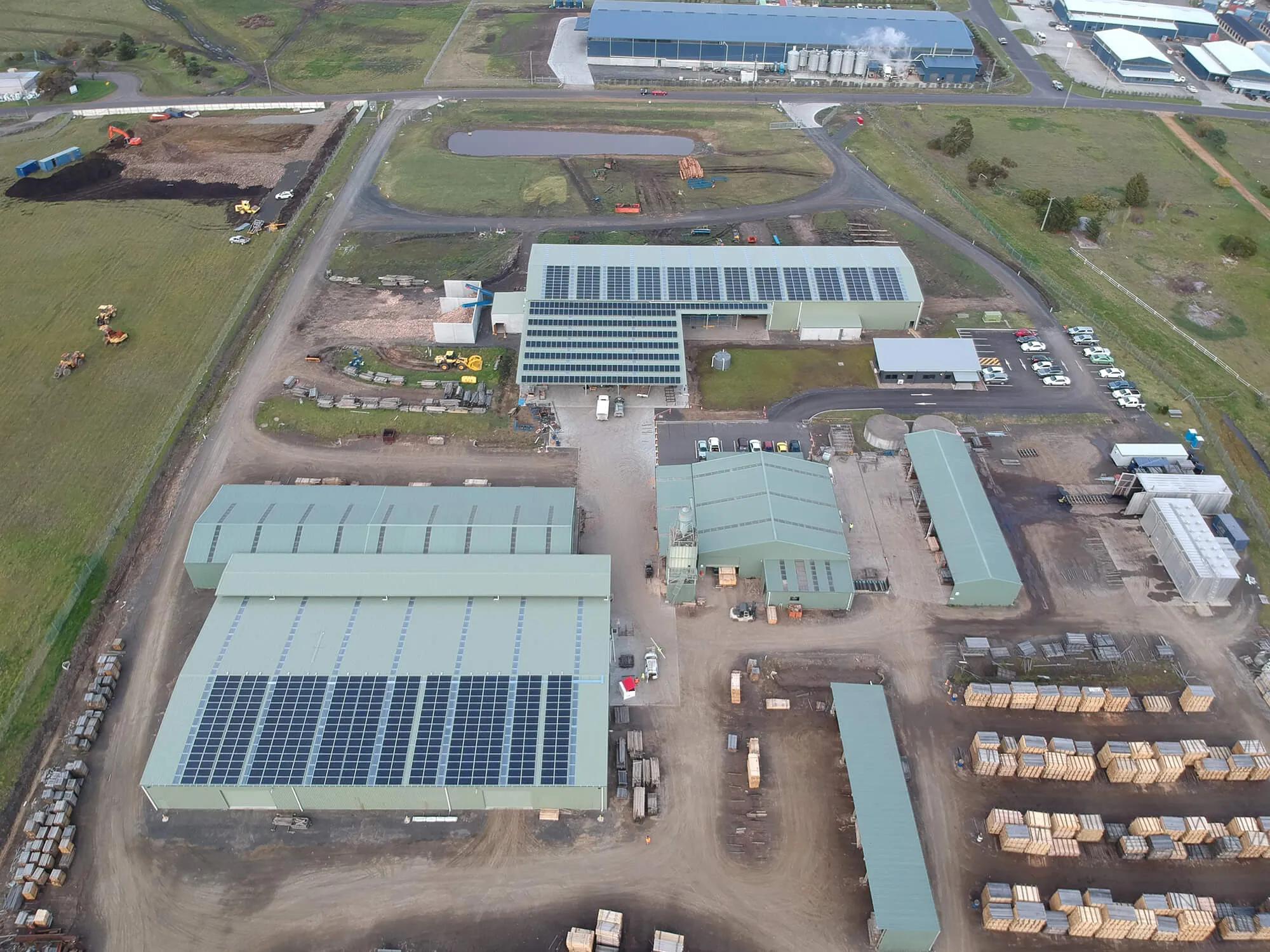 Large building with many windows on ground floor, solar panels attached to roofs of buildings, a large open field in front, multiple trucks parked around perimeter