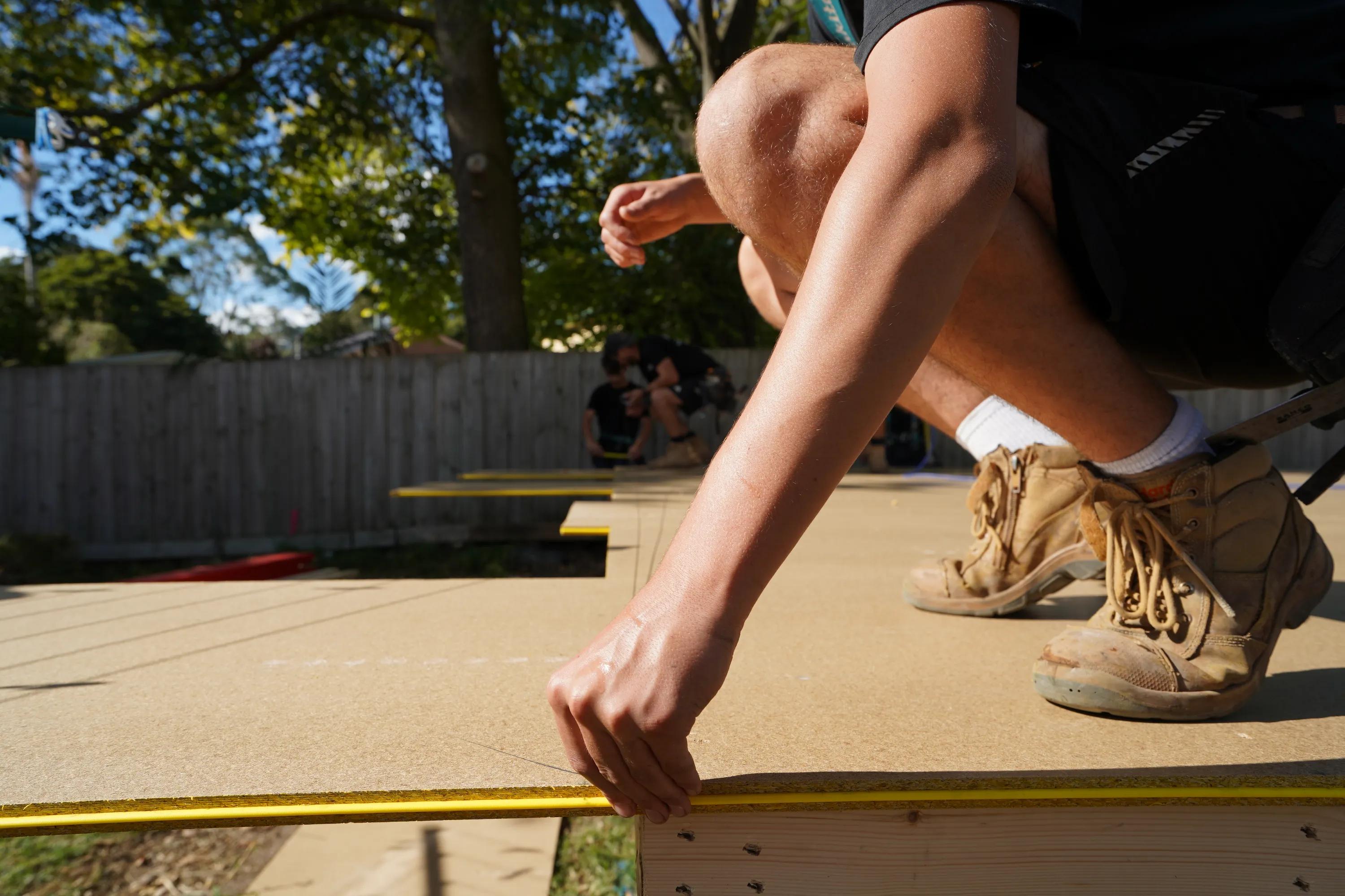 Person installing a timber deck board outdoors while wearing work boots