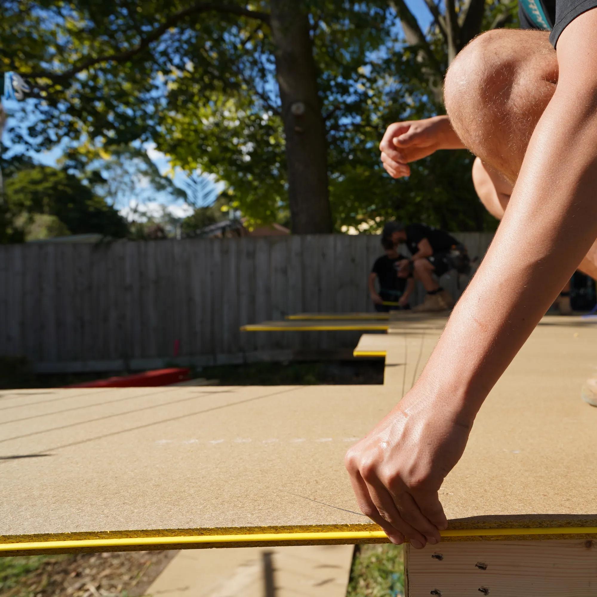 Person installing a timber deck board outdoors while wearing work boots
