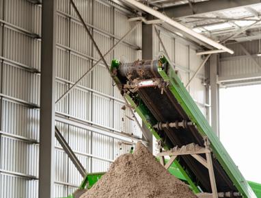 Green conveyor belt depositing processed soil pile inside facility.
