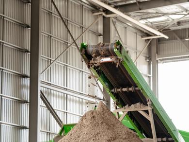 Green conveyor belt depositing processed soil pile inside facility.